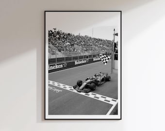 May include: A black and white framed wall art print depicting a Formula One race car crossing the finish line on a track. A checkered flag is visible near the car, with a large crowd of spectators in the background behind a barrier with Heineken text.