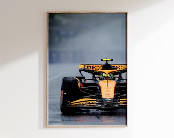 May include: Framed print of a Formula 1 race car in action on a wet track. The car is orange and black, with a driver visible in the cockpit. The background is a blurred, overcast sky, suggesting a rainy race day.