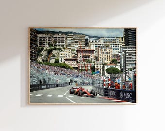 May include: A framed photograph captures a Formula 1 race in Monaco. A red race car speeds along the track, with spectators in the background. Buildings line the course, and the sky is overcast.
