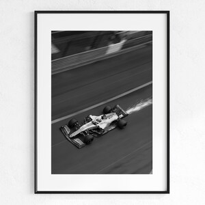 May include: Black and white framed print of a Formula 1 race car speeding along a track. The car is in motion, with motion blur and a trail of water or vapor behind it. The image is a high-angle shot.