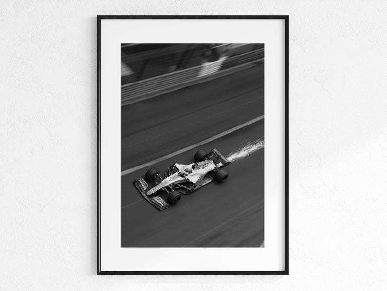 May include: Black and white framed print of a Formula 1 race car speeding along a track. The car is in motion, with motion blur and a trail of water or vapor behind it. The image is a high-angle shot.