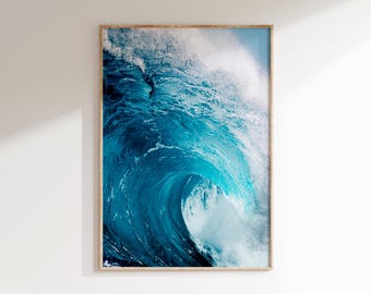 May include: A framed print featuring a dynamic image of a large ocean wave. The wave is captured mid-break, showcasing shades of deep blue and turquoise water with white foam. The artwork is encased in a light-colored wooden frame, suitable for coastal decor.