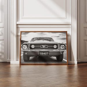 Pode incluir: Impress&atilde;o emoldurada em preto e branco de um cl&aacute;ssico Ford Mustang. O carro est&aacute; centrado, mostrando a frente com far&oacute;is, grelha e placa de matr&iacute;cula "59407". A imagem est&aacute; numa moldura de madeira, contra uma parede branca.