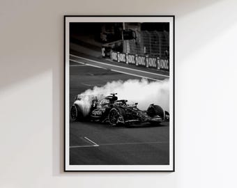 May include: A black and white framed wall art print depicting a Formula 1 race car on a track, emitting a large cloud of smoke from its rear tires. The car features visible sponsor branding and is positioned on the asphalt near a track barrier.