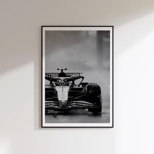Könnte beinhalten: Ein Schwarz-Weiß-Foto eines Formel-1-Rennwagens auf einer nassen Strecke. Das Auto ist von vorne abgebildet und zeigt die aerodynamische Nase, den Cockpitbereich und die breiten Reifen, während es durch den Regen fährt.