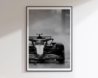 May include: A black and white photograph of a Formula One race car driving on a wet track. The car is captured from a front-facing perspective, showing the aerodynamic nose, the cockpit area, and the wide tires as it navigates through rain.