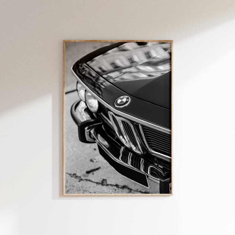 May include: Black and white framed print of a classic car's front end. The image highlights the car's glossy black hood, chrome accents, and the iconic BMW emblem. The car's headlights and grille are also visible.
