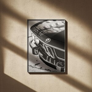 May include: Black and white framed print of a classic BMW car. The image focuses on the front of the car, showcasing the hood, headlights, and iconic BMW emblem. The car's details are highlighted by the monochrome tones.