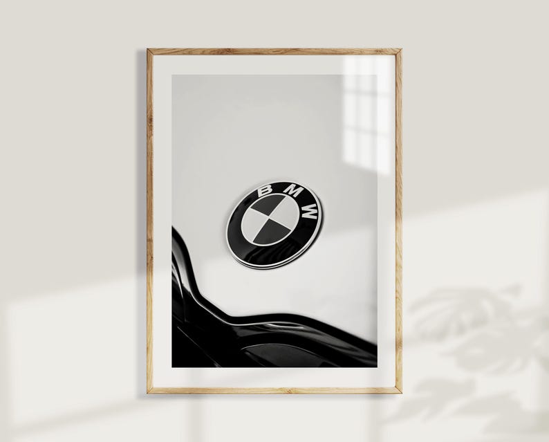 May include: Framed black and white print featuring the BMW logo. The logo is a circular emblem with a black outer ring, a white and blue inner design, and the letters "BMW". The print is in a wooden frame.