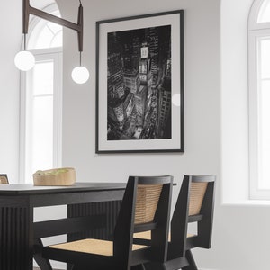 Puede incluir: Impresi&oacute;n en blanco y negro de una ciudad de noche, probablemente Nueva York, con luces brillantes y edificios altos. La impresi&oacute;n est&aacute; enmarcada en una pared blanca sobre una mesa de comedor negra con sillas negras.