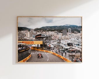 May include: A framed print of a Formula 1 race in Monaco. The image shows a red race car on a track with yellow barriers, surrounded by buildings, boats, and a mountain in the background. The Pirelli logo is visible.