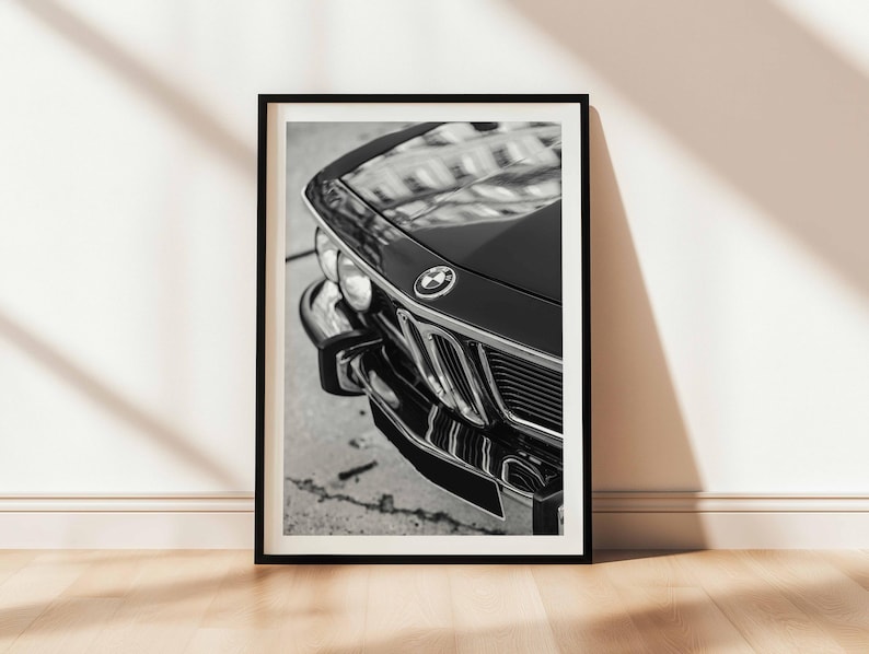 May include: Black and white framed print of a classic car's front end. The image highlights the car's hood, grill, and bumper, showcasing its vintage design. The BMW emblem is visible on the hood.