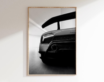 Op de afbeelding: Zwart-wit ingelijste print van een Lamborghini sportwagen. De achterkant van de auto is zichtbaar, met de nadruk op de spoiler, lichten en uitlaat. Het Lamborghini-logo is zichtbaar.