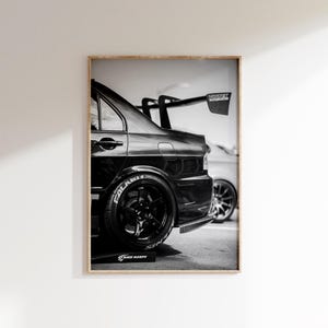 May include: Black and white framed print of a black sports car. The car has a large rear wing and black wheels with white lettering on the tires. The image is a side view of the car.