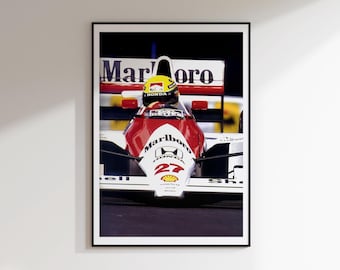 Op de afbeelding: Een ingelijste print van een Formule 1-raceauto, rood en wit, met het Marlboro-logo. De auto heeft nummer 27 en een gele helm. De afbeelding staat tegen een donkere achtergrond.
