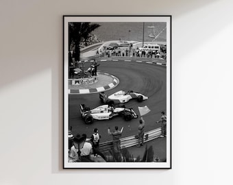 May include: A black and white framed photograph depicting two Formula One race cars navigating a sharp curve on a track. The cars feature visible branding including Marlboro, Canon, and Elf. Spectators stand behind a barrier near the water.