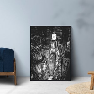 Puede incluir: Impresi&oacute;n en blanco y negro de Times Square por la noche. La imagen captura las luces brillantes y los rascacielos de este emblem&aacute;tico lugar de Nueva York. La obra de arte se exhibe en un sal&oacute;n, apoyada contra una pared.