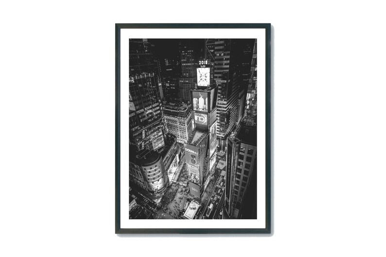 Puede incluir: Impresi&oacute;n en blanco y negro enmarcada de Times Square en Nueva York por la noche. La imagen, tomada desde un &aacute;ngulo alto, muestra vallas publicitarias y edificios iluminados. El a&ntilde;o "2016" es visible en una torre del reloj.