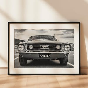 Pode incluir: Fotografia a preto e branco emoldurada de um Ford Mustang cl&aacute;ssico. O carro est&aacute; centrado, mostrando a frente com far&oacute;is, grelha e placa de matr&iacute;cula "59407". A imagem &eacute; exibida num ch&atilde;o de madeira.