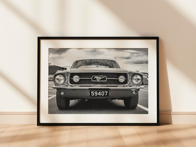 Pode incluir: Fotografia a preto e branco emoldurada de um Ford Mustang cl&aacute;ssico. O carro est&aacute; centrado, mostrando a frente com far&oacute;is, grelha e placa de matr&iacute;cula "59407". A imagem &eacute; exibida num ch&atilde;o de madeira.