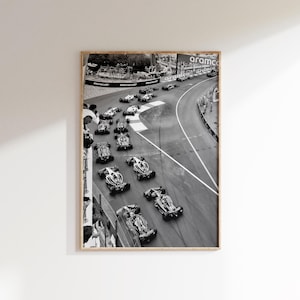 May include: Black and white framed print of a Formula 1 race. The image captures a top-down view of multiple race cars speeding around a track, with spectators visible along the sides. The Aramco logo is visible.
