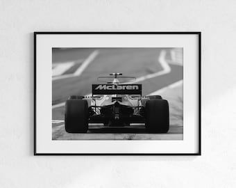 Puede incluir: Impresión enmarcada en blanco y negro de un coche de carreras McLaren de Fórmula 1 en una pista. El coche se ve desde atrás, con el logotipo de McLaren visible. La imagen está en escala de grises.