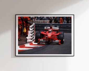 May include: A framed wall art print featuring a bright red Formula One race car on a track. The car displays Marlboro branding and is positioned near a white and black checkered barrier. Pit crew members in red uniforms stand nearby on the asphalt.