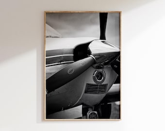 May include: Monochrome photograph of an aircraft propeller and engine. The propeller blades are dark, and the engine is silver with a central light. The image is framed in a wooden border.