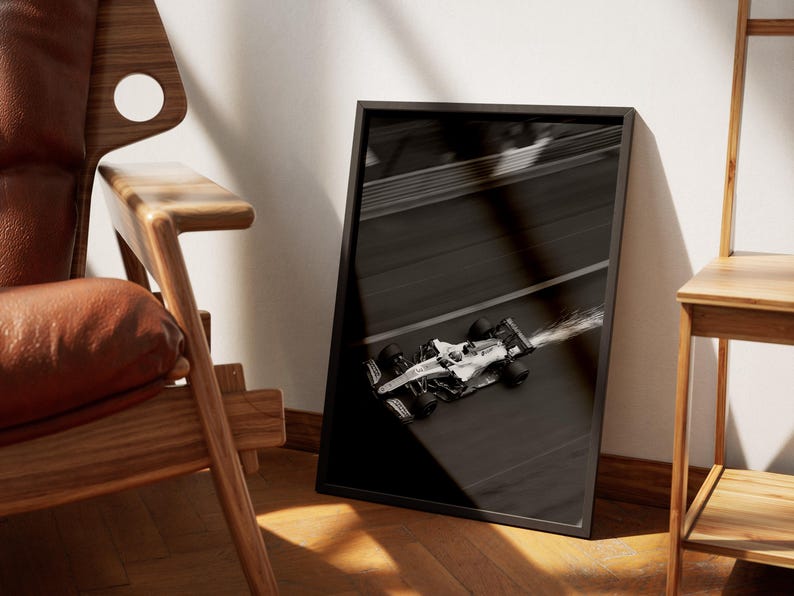 May include: Black and white framed print of a Formula 1 race car speeding on a track. The image is angled, showing the car in motion with a blurred effect, suggesting high speed. The frame is black.