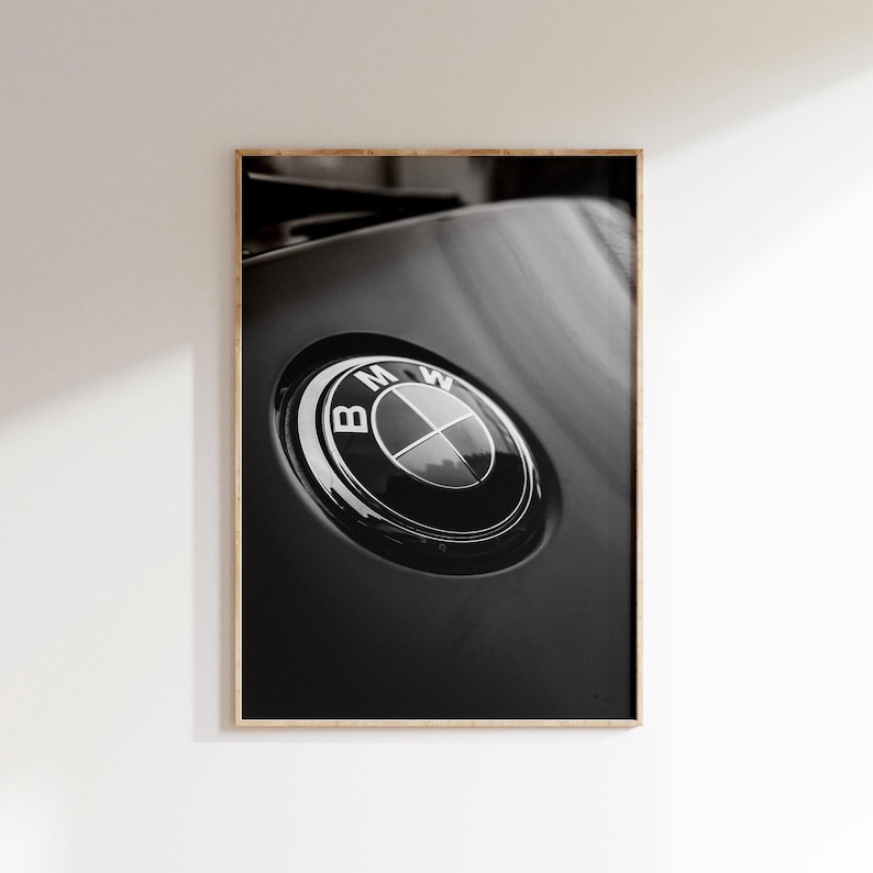Puede incluir: Fotograf&iacute;a en blanco y negro enmarcada con un emblema de BMW. El emblema circular, con su dise&ntilde;o plateado y negro, se encuentra sobre una superficie negra brillante. La fotograf&iacute;a se presenta en un marco de madera.