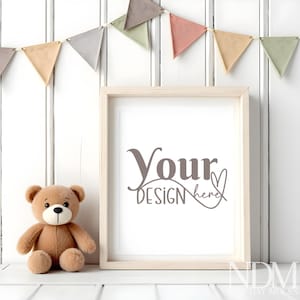 Könnte beinhalten: Ein weißer Bilderrahmen mit einem hellen Holzrahmen steht auf einer weißen Oberfläche. Ein brauner Teddybär sitzt links neben dem Rahmen. Eine bunte Girlande aus Wimpeln hängt über dem Rahmen. Der Rahmen trägt den Text "Your Design here" in Grau.