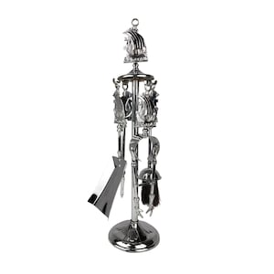 Puede incluir: Un juego de herramientas para chimenea plateado con un soporte. El juego incluye una pala, un atizador, un cepillo y unas pinzas. El soporte tiene una parte superior y una base decorativas. Las herramientas están suspendidas del soporte.