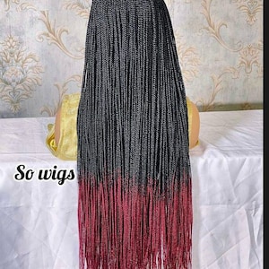 May include: A long black and burgundy ombre braided wig. The wig is styled in small, thin braids. The wig is on a mannequin head.