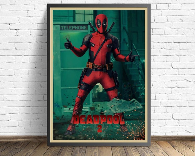 Puede incluir: P&oacute;ster enmarcado de Deadpool con su traje rojo y negro, haciendo una se&ntilde;al de pulgar hacia arriba y se&ntilde;alando. El p&oacute;ster tiene el texto "DEADPOOL 2" en la parte inferior, con una cabina telef&oacute;nica verde en el fondo.