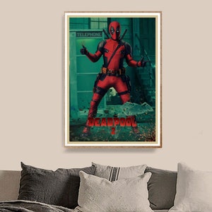 Puede incluir: P&oacute;ster enmarcado de Deadpool con un traje rojo y negro, haciendo una se&ntilde;al de pulgar hacia arriba. El texto "DEADPOOL 2" es rojo. El fondo muestra una cabina telef&oacute;nica y un entorno verdoso.