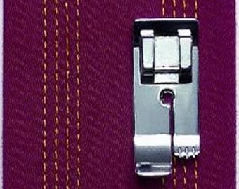 May include: A close-up of a silver sewing machine foot next to a piece of purple fabric with vertical yellow stitching. The foot is made of metal and has a rectangular shape with a small opening. The fabric has a textured appearance.