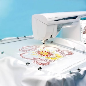 May include: A white Husqvarna Viking sewing machine embroiders a floral pattern in red, yellow, and blue on white fabric. The machine is set against a light blue backdrop. The website address www.sewingmachinesales.co.uk is visible.