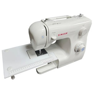 May include: White Singer Tradition sewing machine with a built-in extension table. The machine has a red Singer logo and a variety of stitch settings.