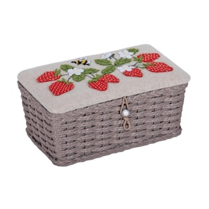 May include: A grey wicker storage box with a linen lid featuring an embroidered design of strawberries, leaves, and a bee. The lid has a brown fabric pull with a pearl-like bead.