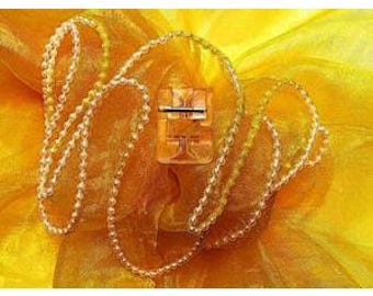 May include: A clear, beaded necklace with a small, clear clasp. The necklace is draped over a yellow, textured fabric. The clasp is centered in the image, with the necklace beads cascading around it. The background is a bright, sunny yellow.