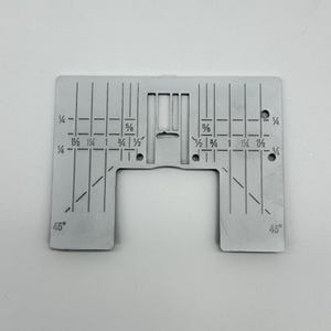 May include: A silver sewing machine needle plate with measurement markings in inches. The plate is rectangular with a cut-out section and angled lines marked at 45 degrees.