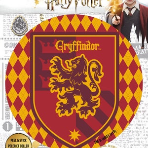 May include: A round, red and gold sticker featuring the Gryffindor house crest from the Harry Potter series. The crest features a lion with a crown above it. The text "Gryffindor" is printed in gold letters on the crest.