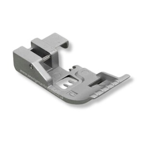 May include: A silver sewing machine foot, likely for hemming or edge finishing. It has a complex design with various components and a needle opening. The website address "www.sewingmachinesales.co.uk" is printed on the foot, which is made of metal.