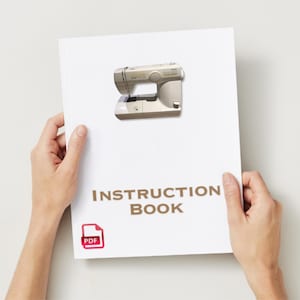May include: A white instruction book with the words "INSTRUCTION BOOK" in brown text. A beige sewing machine is pictured at the top. A red PDF icon is in the lower left corner. The book is held by two hands.