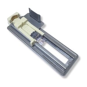 May include: A sewing machine attachment with a silver metal frame and cream plastic parts. The attachment has a rectangular shape with a sliding mechanism and a small, angled metal piece. The text "sewingmachinesales.co.uk" is printed on the frame.