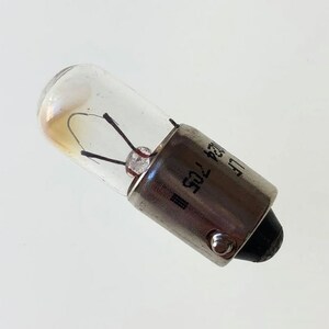 May include: A small, clear glass light bulb with a silver metal base. The base has the text "12V 1.2W" printed on it.