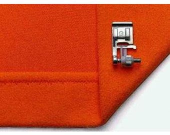May include: A metal sewing machine foot attached to a folded orange fabric. The foot has a silver finish with a screw and a small, angled guide. The fabric is a solid, vibrant orange color.