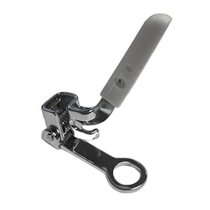 May include: A sewing machine presser foot, with a silver metal base and a grey plastic lever. The foot has a curved design and a small, circular opening at the end. The lever is angled and has a rounded tip.