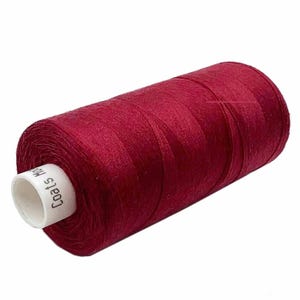 May include: A cylindrical spool of deep red thread. The thread is tightly wound and has a white label with the text "Coats". The thread is a solid, rich colour, suitable for sewing and embroidery projects.