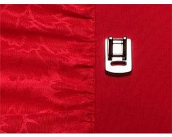 May include: A close-up of a red fabric with a textured pattern on the left and a smooth red fabric on the right. A silver metal sewing machine foot is attached to the smooth fabric.